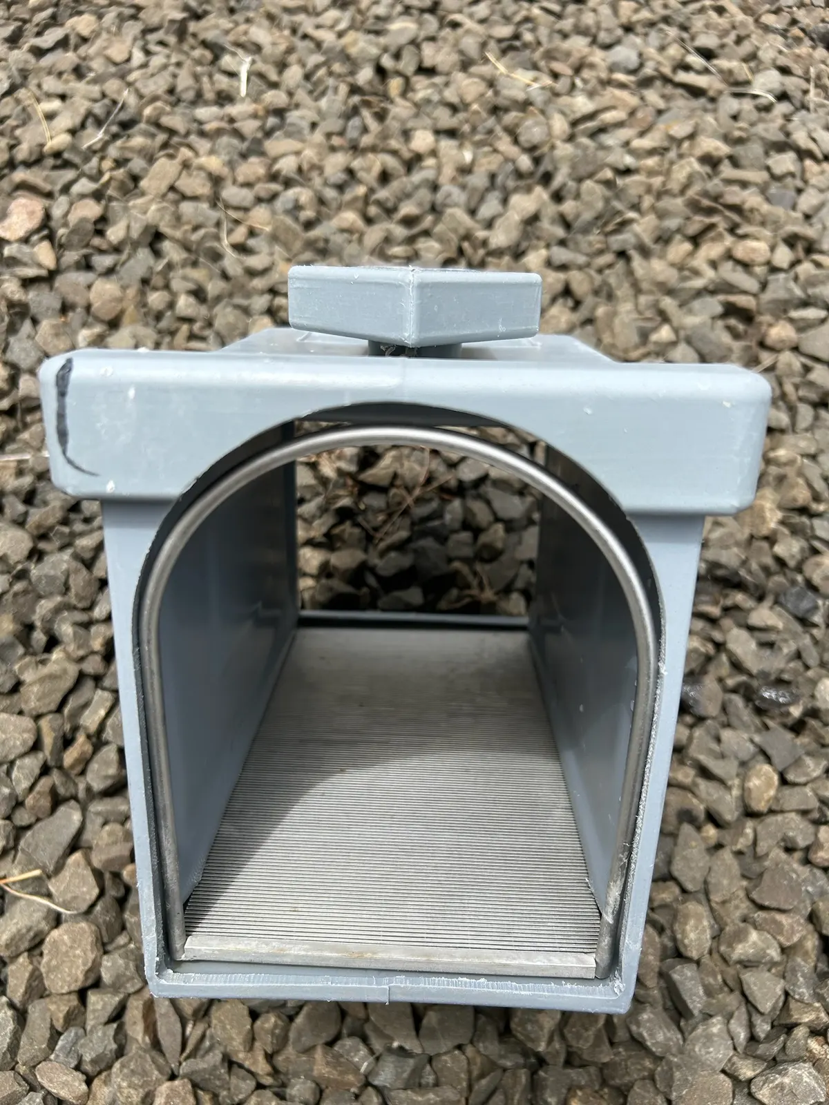 Un regard-filtre gris ouvert, posé sur le gravier.