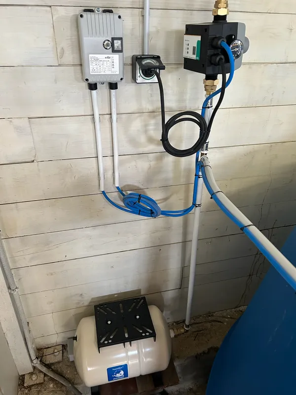 Le surpresseur, son vase d’expansion et le coffret de commande fixés au mur, tuyaux bleus.