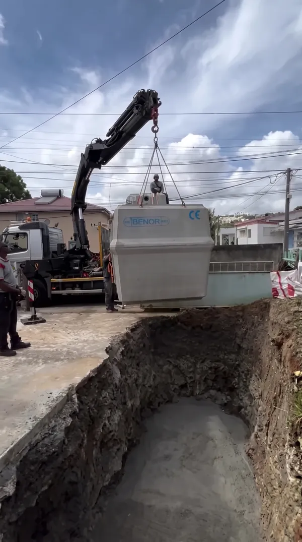 Grue déposant un décanteur primaire en béton de 3 tonnes dans une fosse d'assainissement.