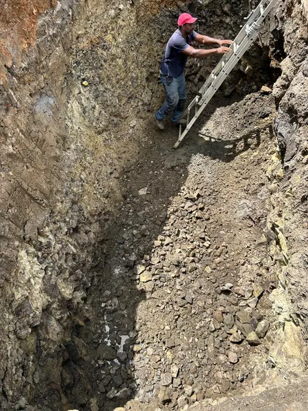 Un technicien sur une échelle au fond de la fouille, parois de terre et de roche.