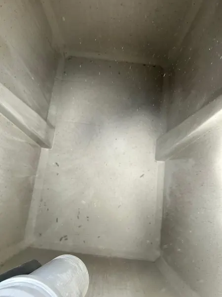 L’intérieur d’une cuve en béton, parois lisses, une canalisation blanche en bas.