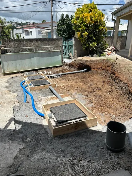 Des coffrages en bois autour des regards, un tuyau bleu et une canalisation grise raccordés.