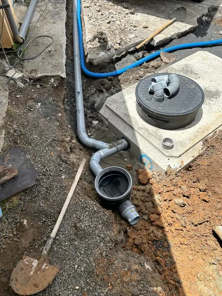 Des canalisations grises et un tuyau bleu raccordés à un regard, dans la tranchée.