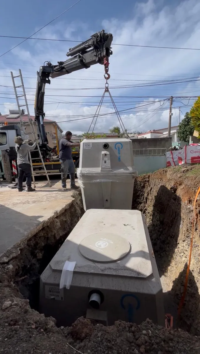 Sur un de nos chantiers : la micro-station suspendue à la grue, deux techniciens la guident dans la fouille.